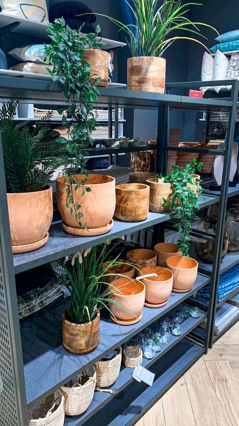 Plantas artificiales y decoración del hogar dispuestas en estanterías de tienda.