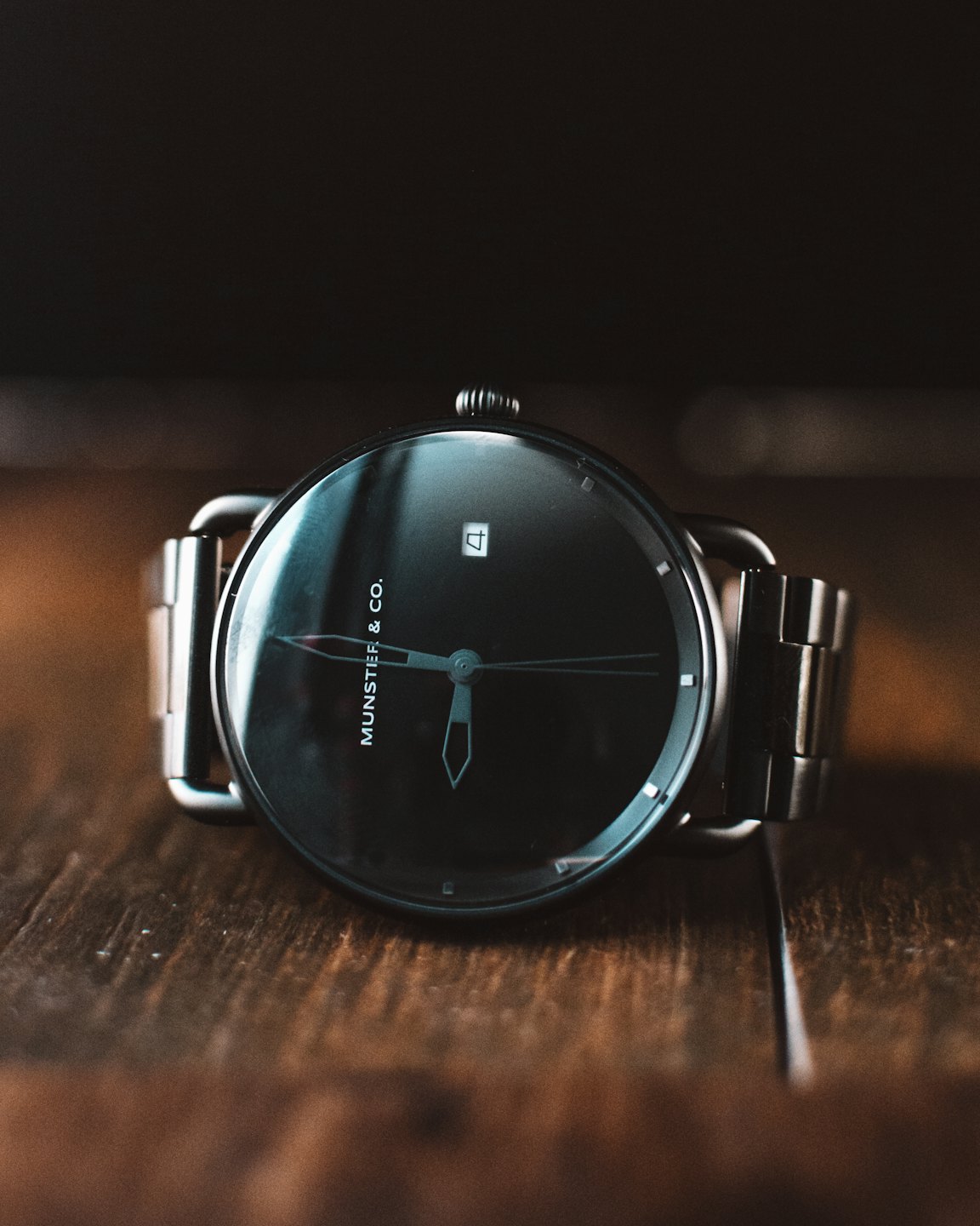 Reloj de pulsera moderno con correa de metal sobre una mesa de madera.
